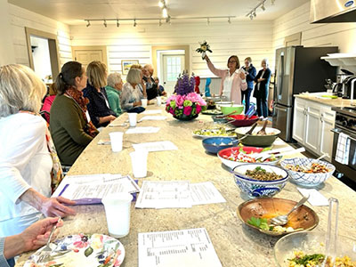 A group of women seated at a long kitchen bar with food and flower arrangements
